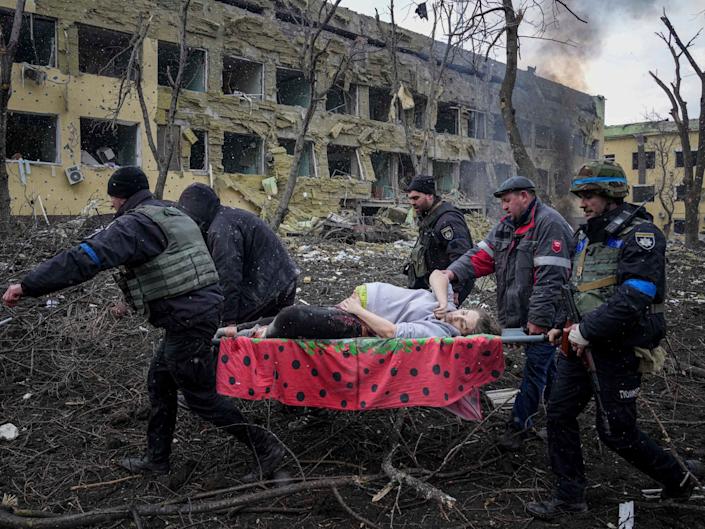Ukrainian emergency employees and volunteers carry an injured pregnant woman.